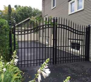 A black ornamental iron overscallop estate gate next to the side of the house