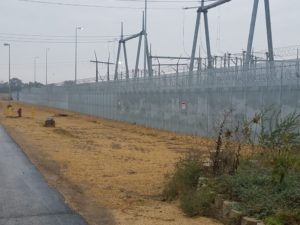 A high security fence with large industrial features laying beyond it