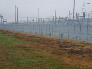 A distance shot of a high security fence with large industrial features laying beyond it