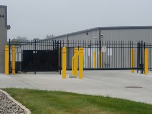 An ornamental iron cantilever gate with a keypad and gate operator surrounded by bright yellow traffic pillars for protection