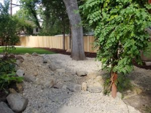 A dry river bed feature installed with large and small stones, greenery and a stone retaining wall