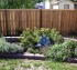 A small garden with a few varieties of flowers with an alternating board custom wood fence stationed a few feet behind it