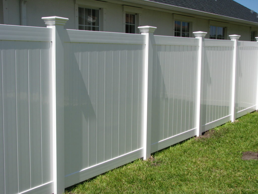 A diagonal shot of a solid white vinyl privacy fence cutting across a green lawn