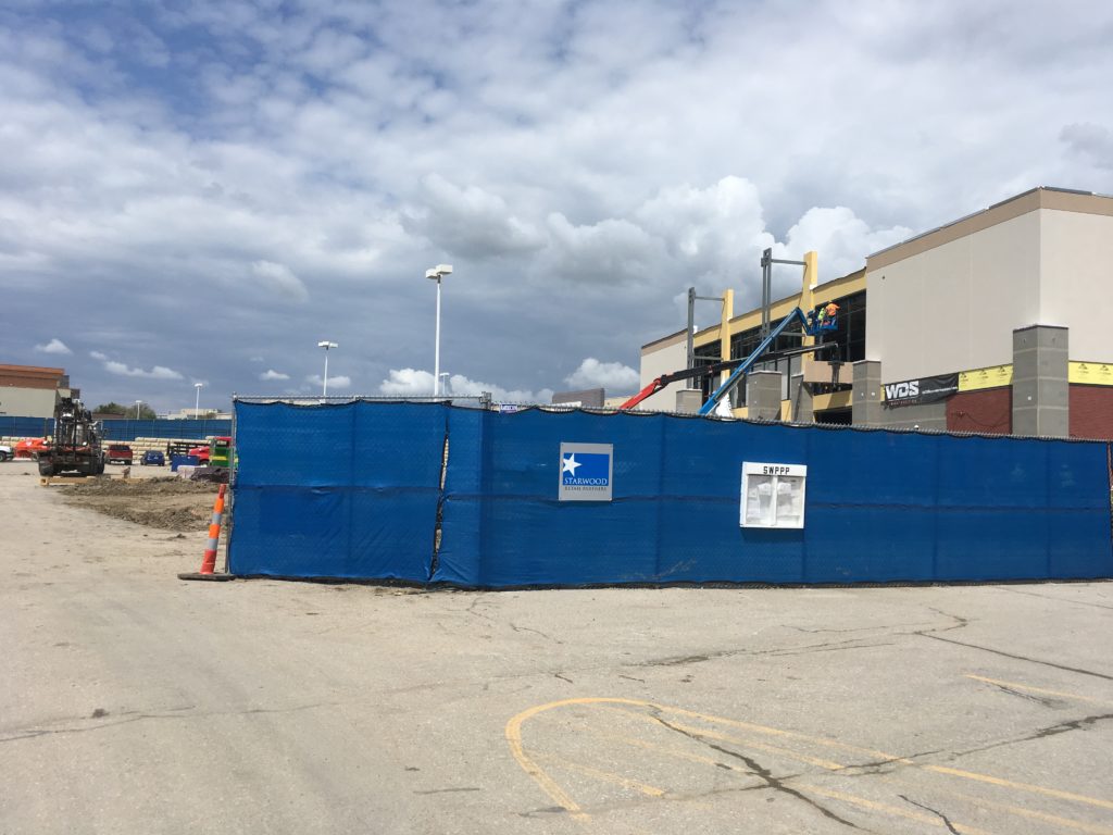 Rental fence with a blue windscreen installed in front of a construction site to reduce visibility and debris transference