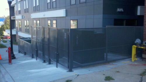 6 - 8 foot black woven and welded wire fence creating an enclosure around outdoor power boxes on cement