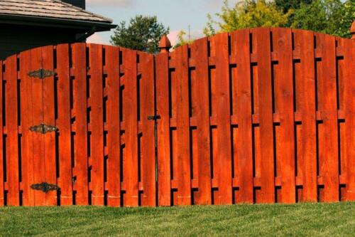 6-8 foot tall red overrscalloped pattern shadowbox wooden fence with similarly styled single swing gate