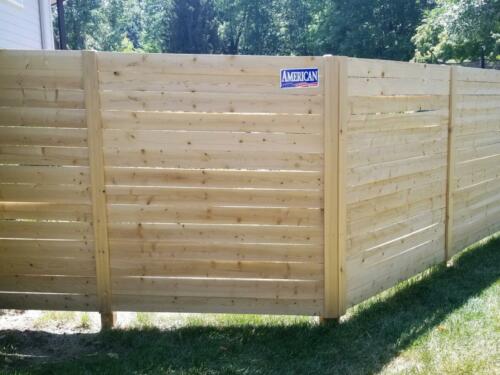 6-8 foot tall horizontal wooden fence with wooden vertical fence posts, fence baseline is 2-5 inches off of ground-level