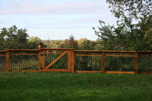 2-4 foot decorative wooden railing with a similar single swing gate that staggers to accommodate uneven grass terrain that also goes around a small platform overlooking a lake