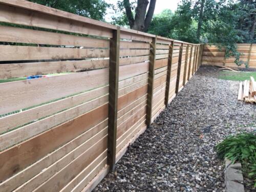 6-8 foot tall horizontal wooden fence with hidden off-colored post and inward beveled top of fence