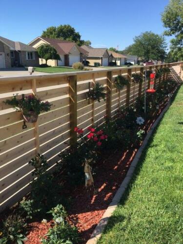 6-8 foot tall horizontal wooden fence with off-colored post with inward overhang and plants hanging on fence gaps