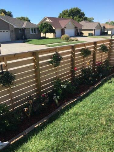 6-8 foot tall horizontal wooden fence with off-colored post with inward overhang and plants hanging on fence gaps