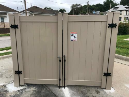 6 - 8 foot tall tan vinyl fence with manual swing gates creating a small enclosure