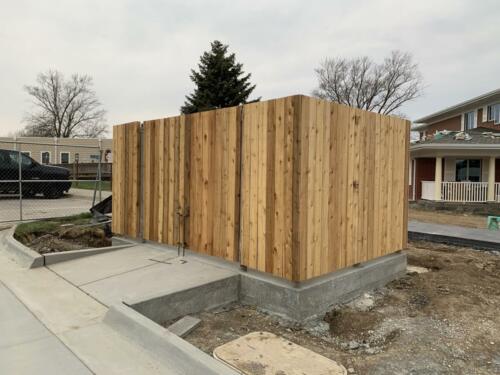 6 - 8 foot tall wood fencing with two swing gates atop a cement surface creating an enclosure