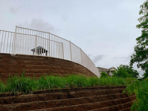 4 - 5 foot tall curved white railing around top of a retainer wall