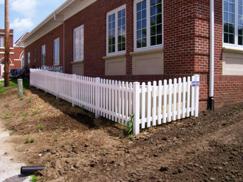 3 - 5 foot tall white vinyl fence going alongside and connecting with brick building