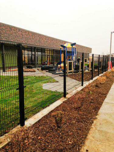 6 - 8 foot black woven and welded wire fence creating an enclosure around a playground
