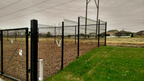 6 - 8 foot black woven and welded wire fence with a swing gate creating an enclosure