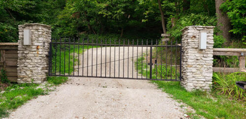 6 - 8 foot tall black automated swing gate attached to two stone columns
