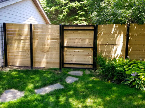 6-8 foot tall horizontal wooden fence with black metal fence posts and a similar reinforced single swing gate