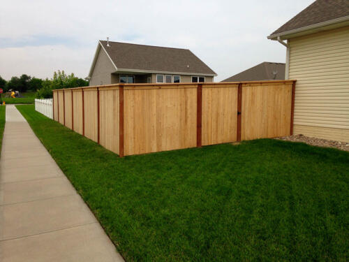 6-8 foot tall wooden privacy fence with off colored fence posts and outward beveled top with similarly styled single manual swing gate