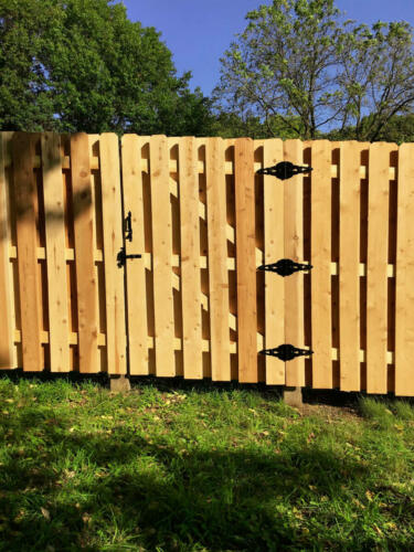 6-8 foot tall shadow box wooden fence with similarly styled single swing gate enclosing a yard