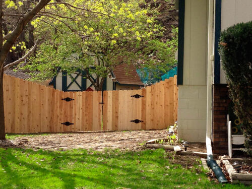 4-6 foot tall wooden privacy fence enclosing a yard that gradually decreases height with similarly styled 3-5 foot tall double swing gate