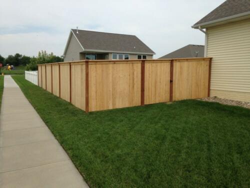 6-8 foot tall wooden privacy fence with off colored fence posts and outward beveled top with similarly styled single manual swing gate
