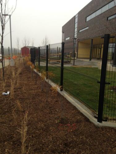 6 - 8 foot black woven and welded wire fence creating an enclosure along a large brick building