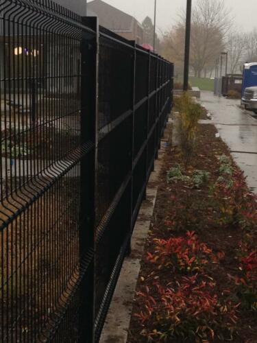 6 - 8 foot black woven and welded wire fence creating an enclosure along a flowerbed