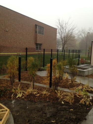 6 - 8 foot black woven and welded wire fence creating an enclosure along a large brick building