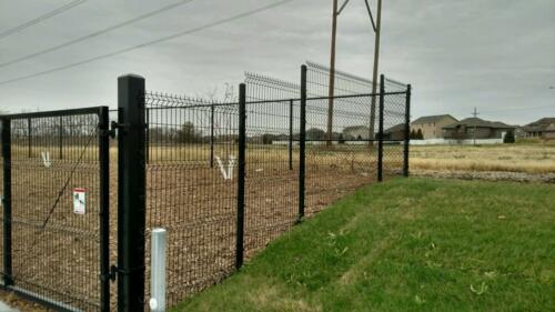 6 - 8 foot black woven and welded wire fence with a swing gate creating an enclosure