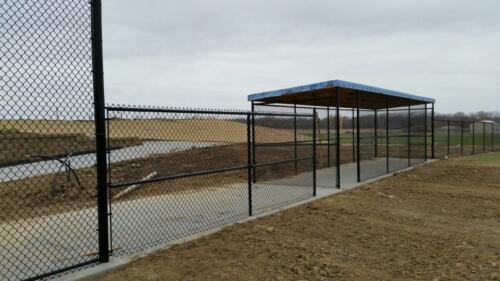 4- 8 foot black fenced in dugout on a field that is undergoing landscaping